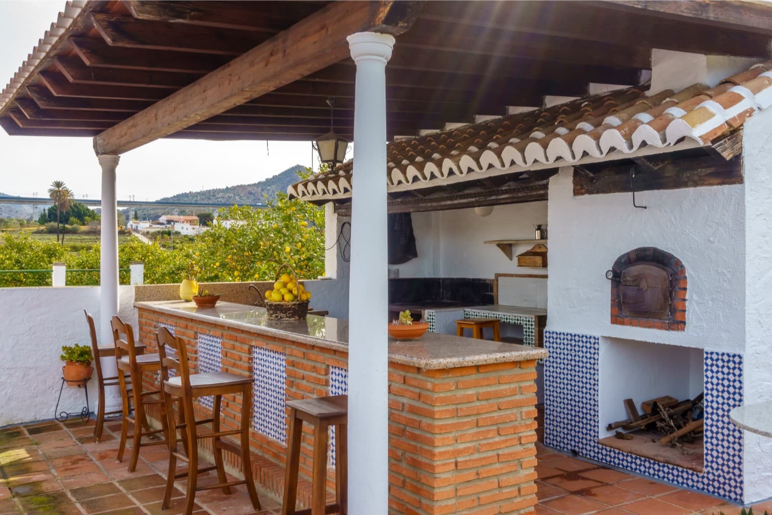 Sunny outdoor bar area featuring rustic wooden stools and brick architecture.