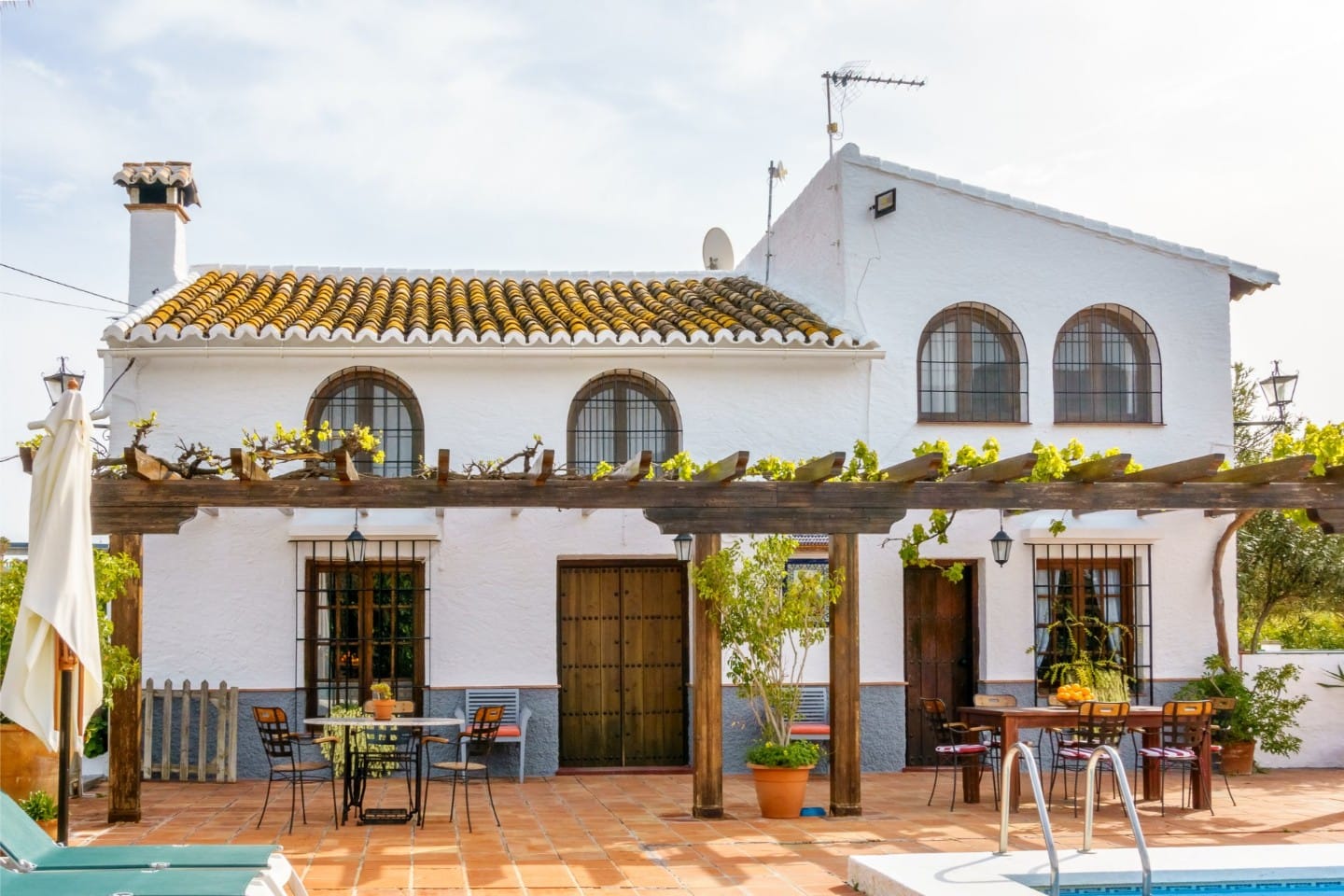 Sun-drenched front terrace with a wooden pergola and outdoor dining table.
